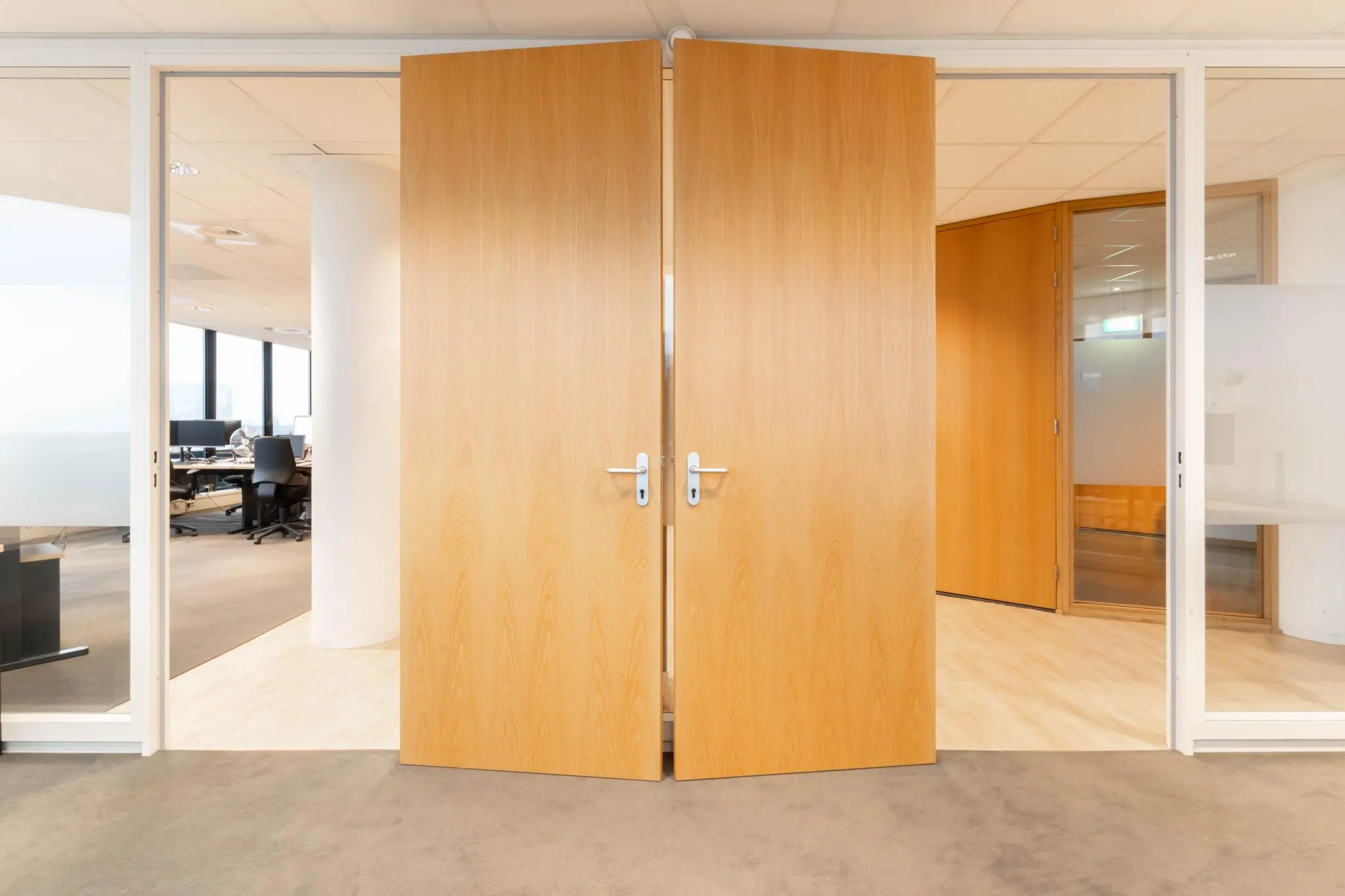 Dubbele houten deuren openen naar een modern kantoorpand aan de 1e Hogeweg, met zicht op werkplekken en glazen wanden.